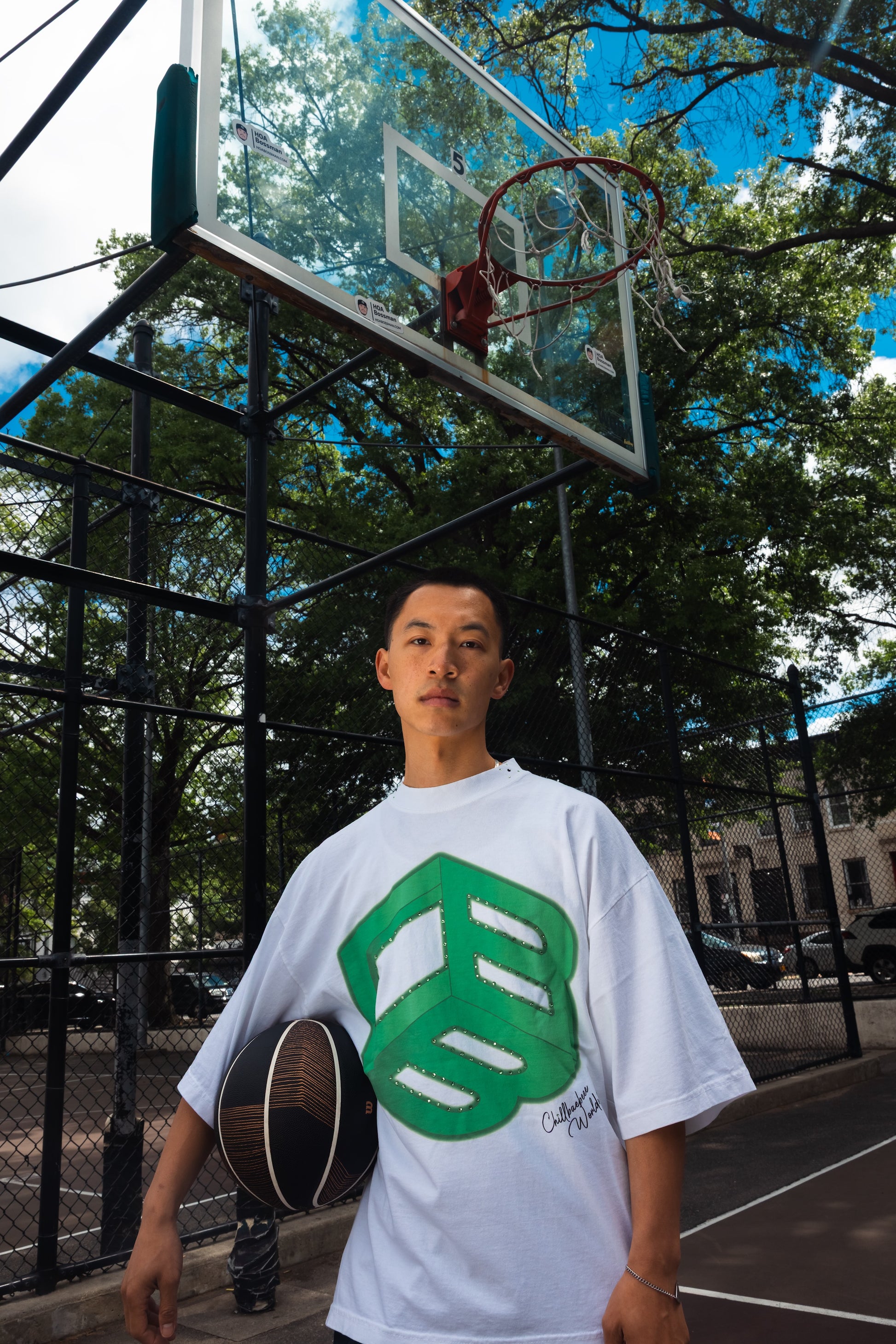 Model wearing white CHILLBAEBEEE Men's Tee with green CBB logo on an outdoor basketball court