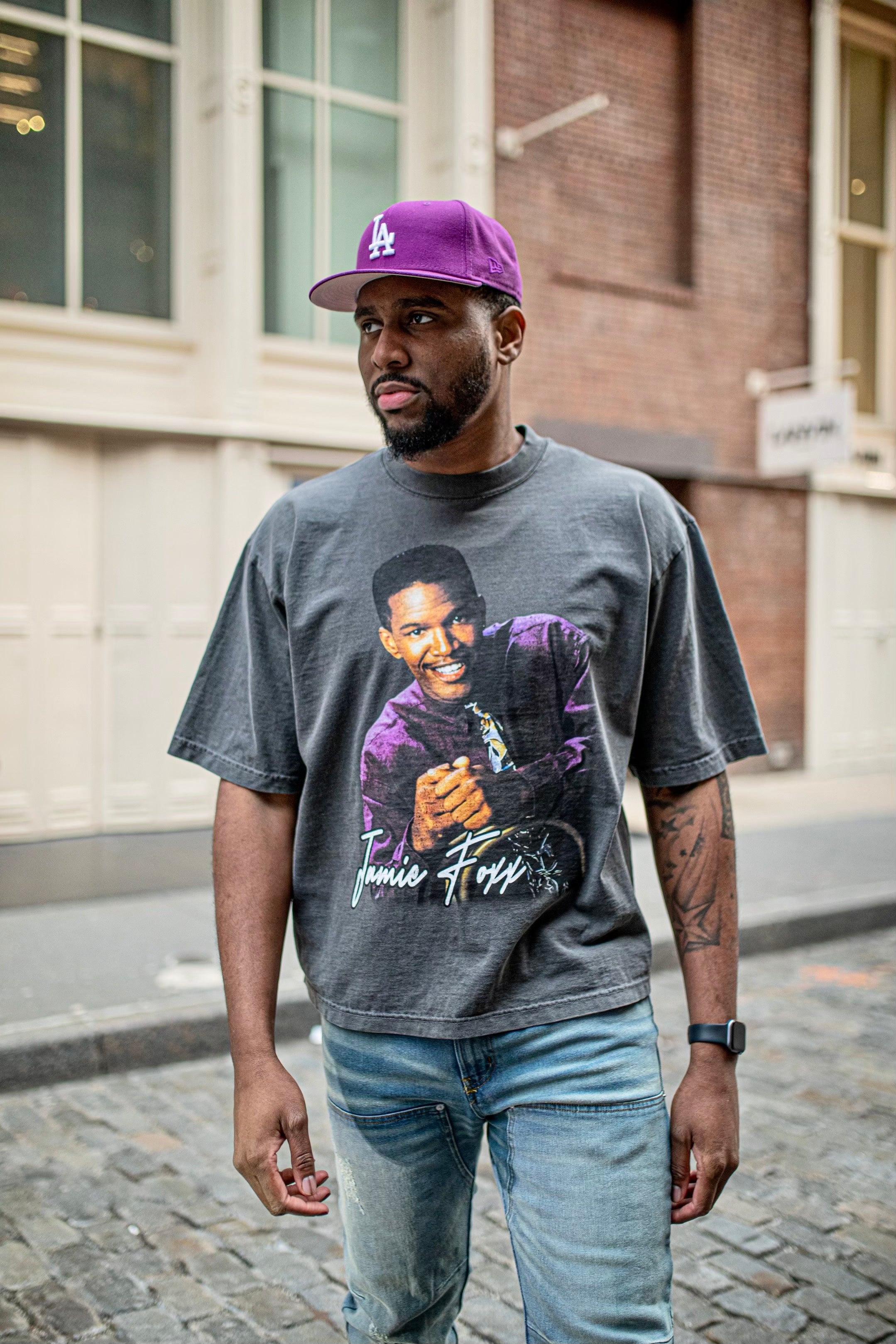 Model wearing grey CHILLBAEBEEE Jamie Foxx graphic tee and cap, standing on a city street